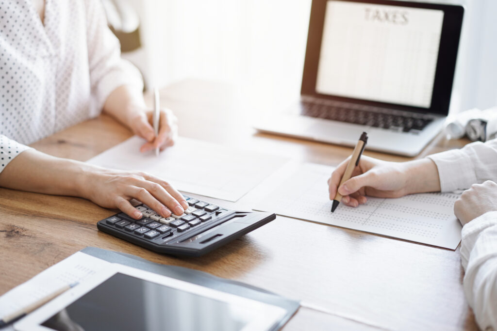 Two accountants using a laptop computer and calculator while doing payroll